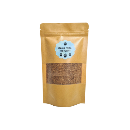 Ozola mizas pulvera iepakojums (amatnieku papīra stāvpaka) ar caurspīdīgu lodziņu un zilu etiķeti ar tekstu "Ozola miza." (latviski) un "Кора Дуба." (krieviski), izolēts uz balta fona.